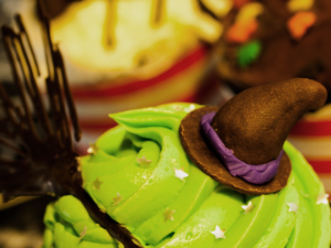 Imagem ilustrativa de um sorvete verde limão. Na esquerda tem uma vassoura feita de chocolate e, na direita, um chapéu marrom de bruxa, também de chocolate.