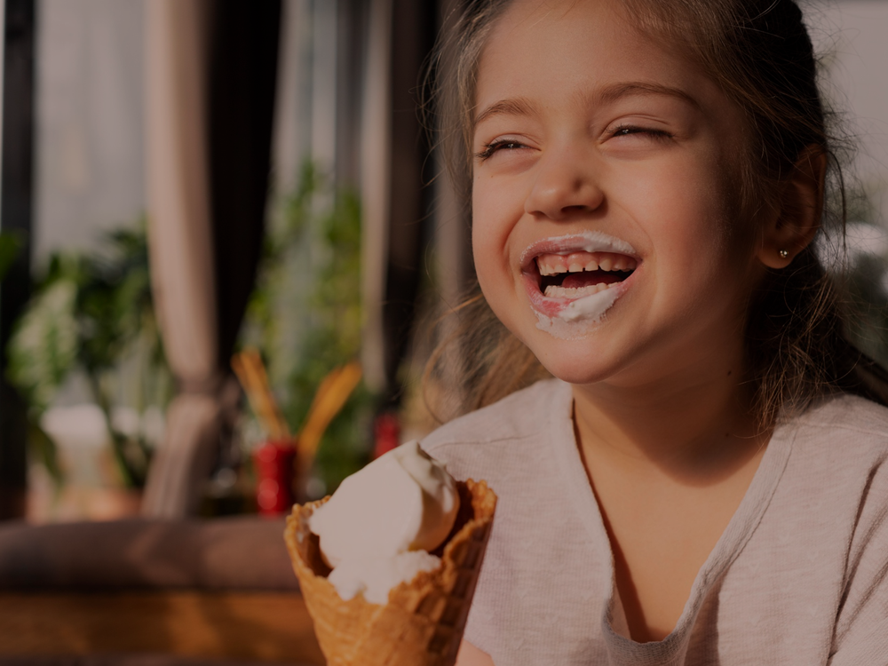 Fotografia ilustrativa de uma criança tomando sorvete, sorrindo e com a boca lambuzada - smothie de café com chocolate